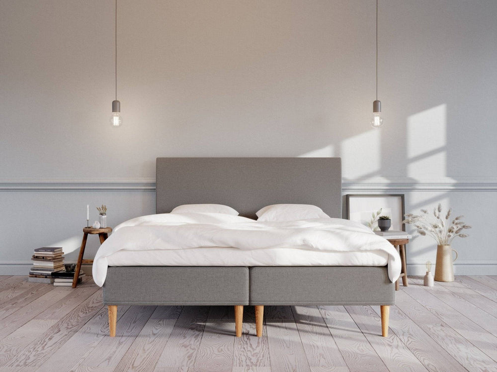 Grå Saga boxmadras 180x200 med polstret gavl, træben og hvidt sengetøj i lyst, minimalistisk soveværelse