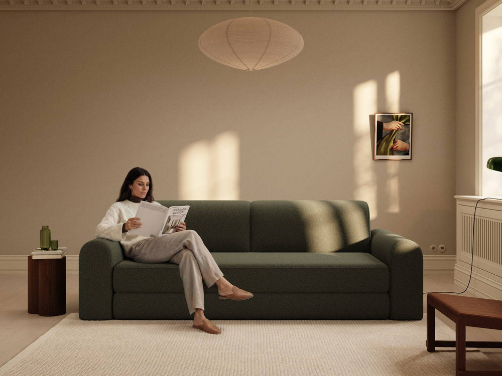 Grøn bouclé sovesofa 200x200 cm, bløde afrundede armlæn og ryglæn i roligt stueinteriør, person sidder læsende på sofaen