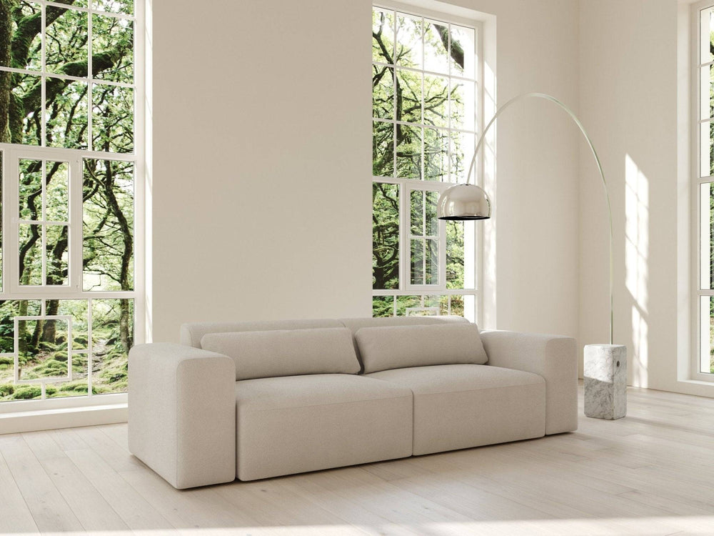 Sofabed i bouclé-creme, lavt modulært design med bløde armlæn og ryglæn i lyst minimalistisk rum foran store vinduer