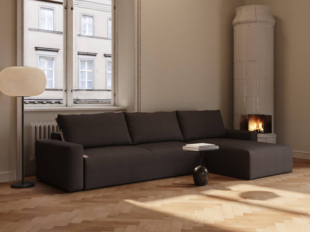 Mørk chokoladebrun sovesofa med chaise longue, bløde stofhynder og lave armlæn i lyst, minimalistisk stueinteriør.