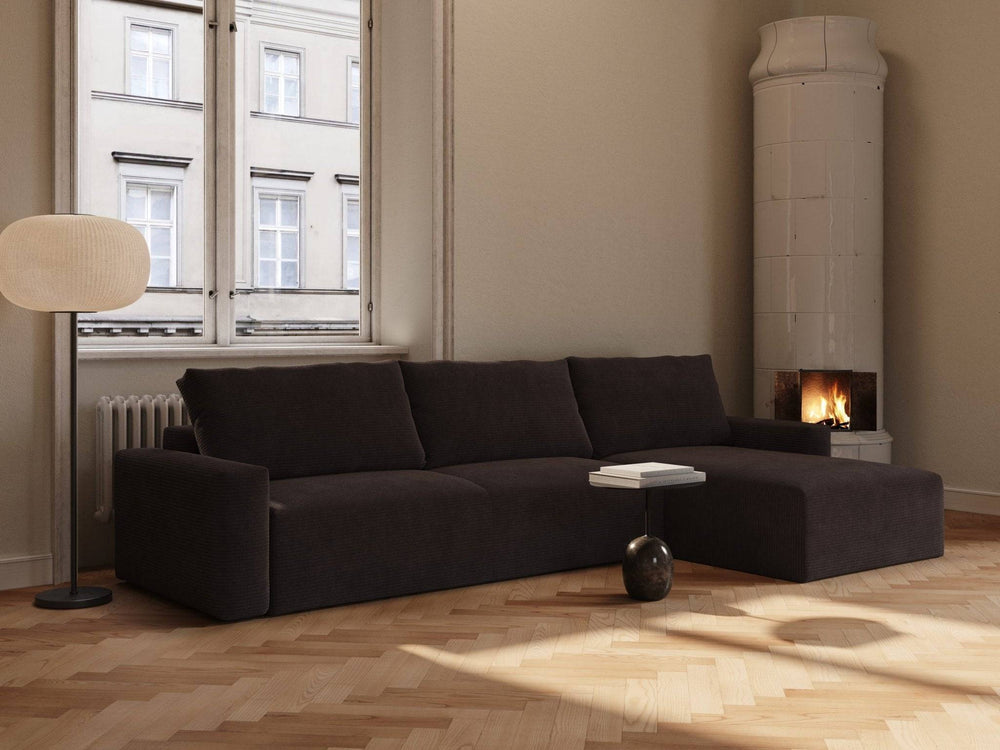 Mørk chocco fløjl sovesofa med chaiselong, bløde puder og lavt sofabord i lyst, minimalistisk stueinteriør.