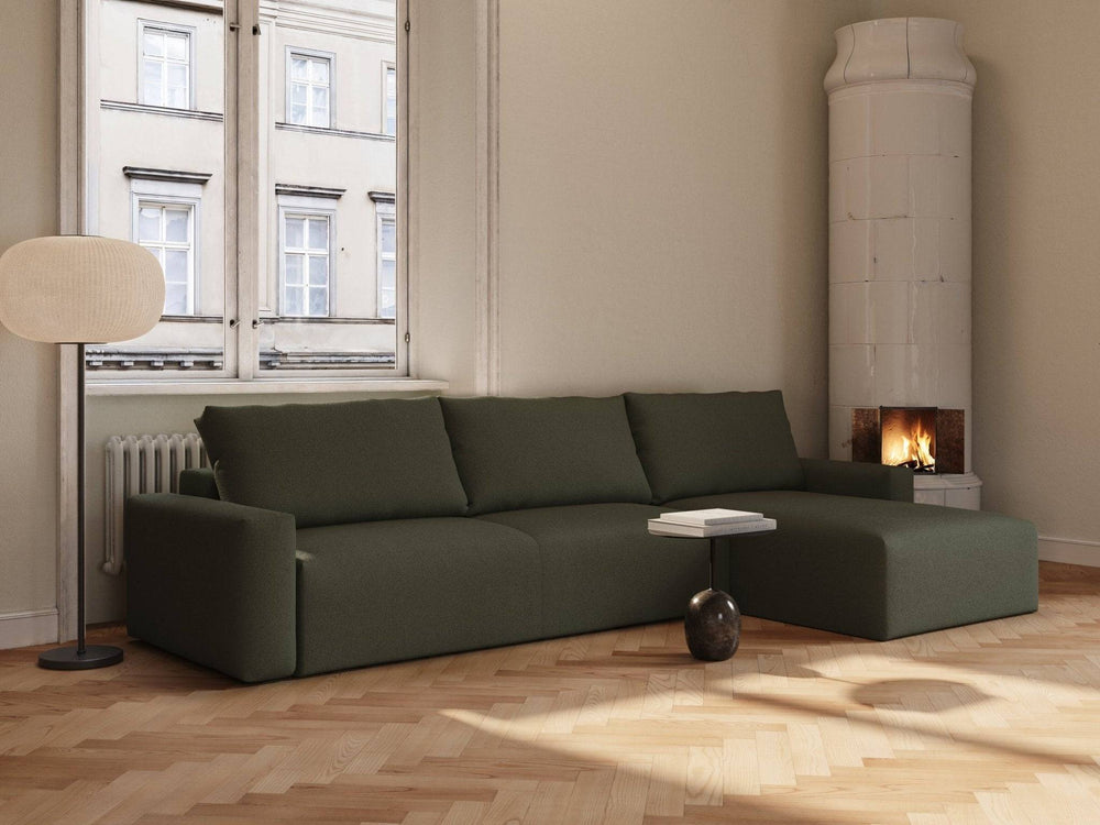 Grøn bouclé sovesofa med chaiselong, lave armlæn og tre rygpuder i lyst, minimalistisk stueinteriør.