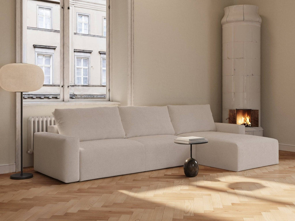 Ivory fløjl sovesofa med chaiselong, lys beige ribstruktur, bløde puder, hjørneopstilling i lyst rum ved vindue og pejs