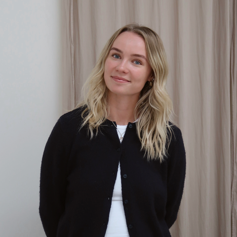 nærbillede af blonde hår, lyseblå øjne og sort uldcardigan foran beige gardin