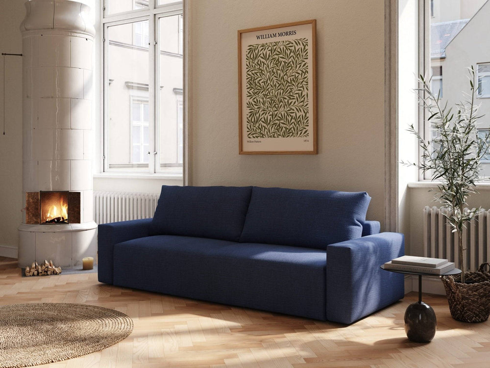 Mørkeblå Mara sovesofa 145x200 cm i tekstil, bløde puder og rene linjer i lyst stueinteriør ved pejs.