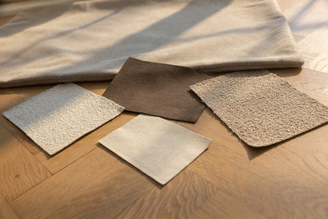 Udsnit af naturfarvede stof- og tæpperprøver i beige og brune nuancer på lyst trægulv