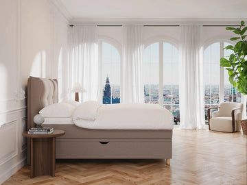 Kontinentalseng "Alva" 160x200 i mocha stof, polstret hovedgærde, hvidt sengetøj i lyst, elegant soveværelse.