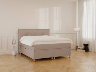 Beige/brun kontinentalseng 160x210 med polstret hovedgærde, hvid dyne og enkle træben i lyst, minimalistisk soveværelse