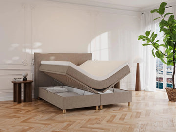 Kontinentalseng Alva 160x200 i latte bouclé med løftbar topmadras og opbevaringsrum, naturfarvet stof og gyldne ben.