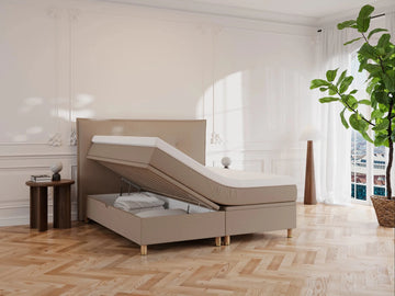 Brun kontinentalseng "Alva" 160x200 med løftbar topmadras og opbevaringsrum, beige stof, høj ryg, lyst trægulv og planter