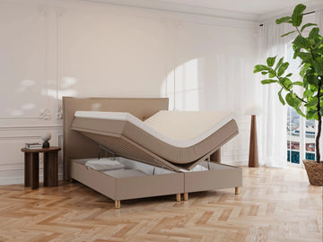 Brun kontinentalseng Alva 160x200 med løftbar topmadras og opbevaringsrum, beige stof, træben på lyst parketgulv.