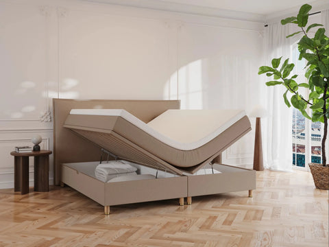 Brun kontinentalseng "Alva" 200x200 med løftbart topmadrasselager, beige betræk, opbevaring og lyst trægulv.