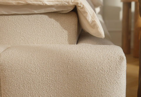 Nærbillede af beige bouclé-stof på sengekant med cremefarvet dyne, blødt rustikt tekstil og afrundede kanter