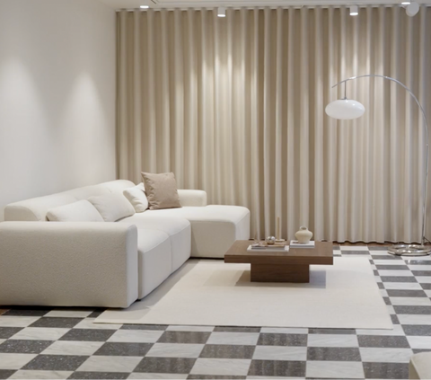 Lys beige stofsofa med bløde puder, træ-sofabord, keramiske dekorationsobjekter og bølgede beige gardiner.