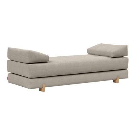 Beige polstret daybed i linnedlignende stof med lave træben og to løse rygpuder, minimalistisk design.