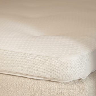 Nærbillede af en Topmadras Fjord | 90x210 med en tekstureret overflade på en seng. Stoffet er blødt og polstret for en forbedret søvnoplevelse, med subtile quiltningsmønstre og mesh-lignende færdige kanter.